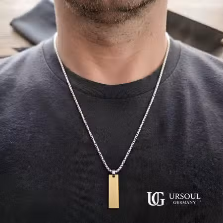 Cadena plateada con dije de placa dorada para hombre, Colección Gold Color Ursoul Germany, sobre camiseta negra