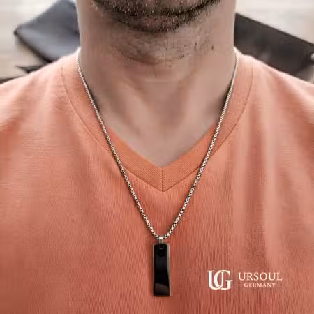 Cadena plateada con dije de placa negra para hombre, Black Series Ursoul Germany, sobre camiseta terracota