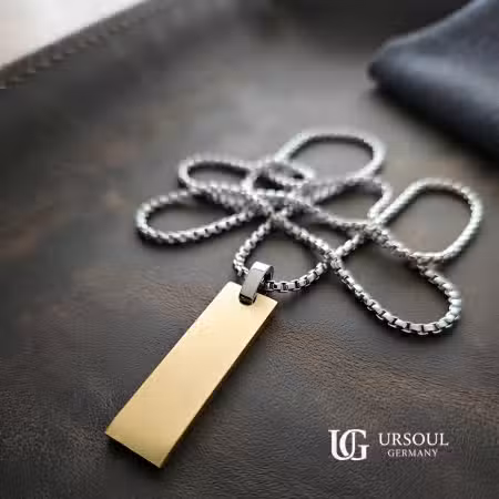 Cadena plateada con dije de placa dorada para hombre, Colección Gold Color Ursoul Germany, sobre camiseta negra