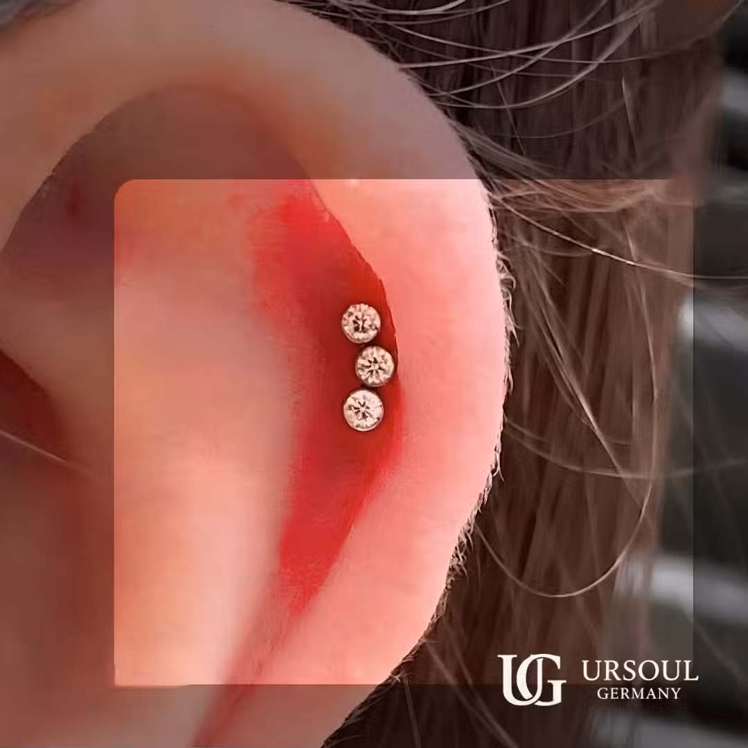 Damas nuevo logo (2) Piercing triple cristal dorado 8mm en cartílago para mujer, Gold Color Ursoul Germany, sobre dedo y fondo negro con detalle de rosca interna