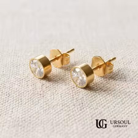 ar de aretes solitario dorados con cristal 6mm para hombre, Gold Color Ursoul Germany, sobre tela texturizada beige
