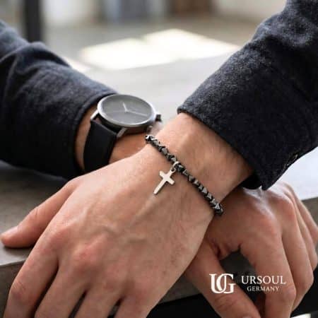 Pulsera de cuentas hematita facetada negra con cruz plateada colgante para hombre, Black Series Ursoul Germany, sobre muñeca con reloj y saco gris