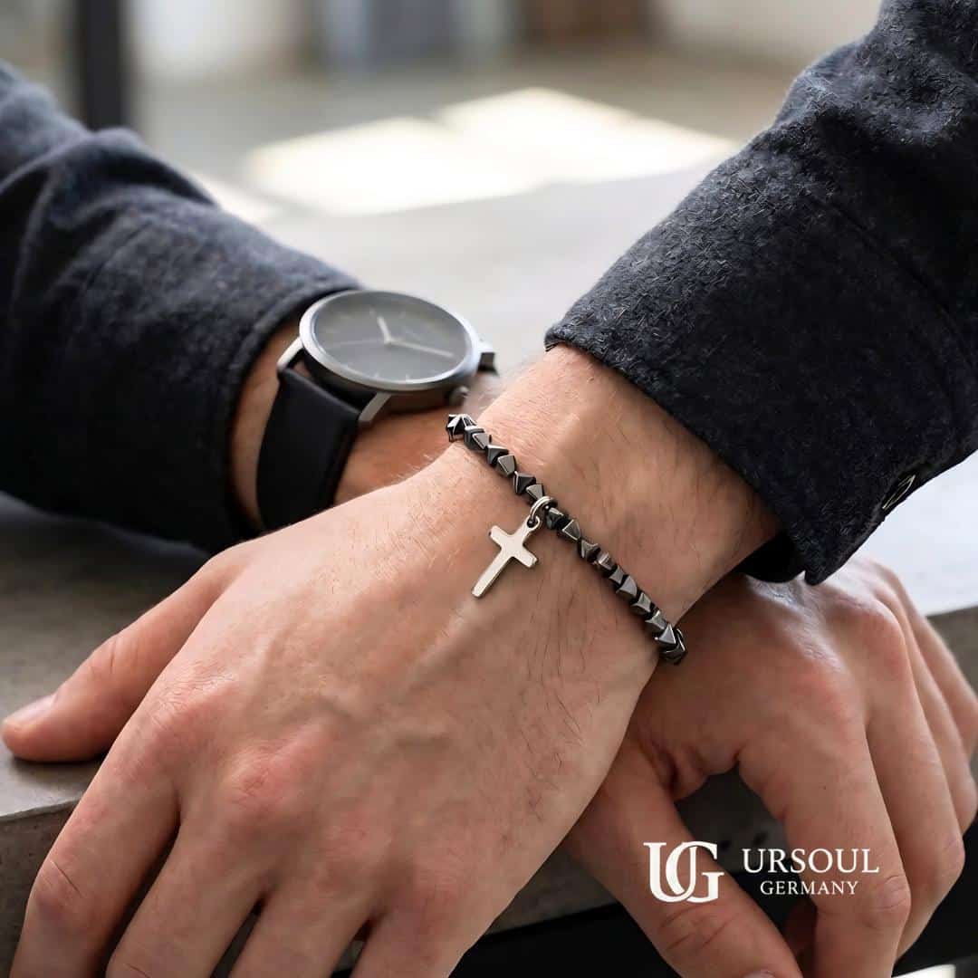WhatsApp Image 2026-08-15 at 9.52.21 AM (4) Pulsera de cuentas hematita facetada negra con cruz plateada colgante para hombre, Black Series Ursoul Germany, sobre muñeca con reloj y saco gris