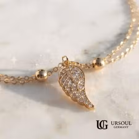 Collar cadena dorada con dije ala de ángel cubierta de cristales para mujer, Gold Color Ursoul Germany, sobre mármol blanco