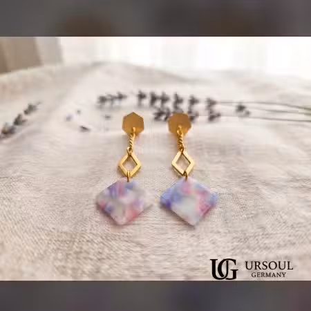 Aretes colgantes hexágono dorado con placa mármol lila para mujer, Gold Color Ursoul Germany, sobre tela beige con lavanda y en oreja con fondo de jardín