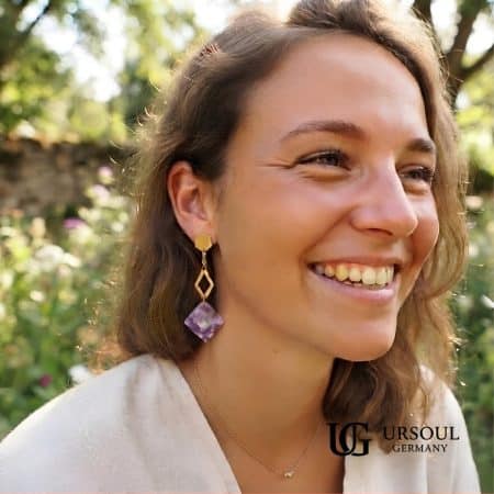 Aretes colgantes hexágono dorado con placa mármol lila para mujer, Gold Color Ursoul Germany, sobre tela beige con lavanda y en oreja con fondo de jardín