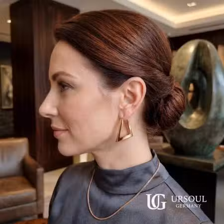 Aretes triángulo rosegold para mujer, Rosegold Color Ursoul Germany, en mano sobre mesa de madera y en oreja con recogido elegante en ambiente de lujo