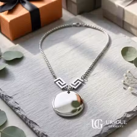 Collar medallón circular plateado con llave griega para mujer, Silver Plated Ursoul Germany, sobre pizarra gris con cajas de regalo