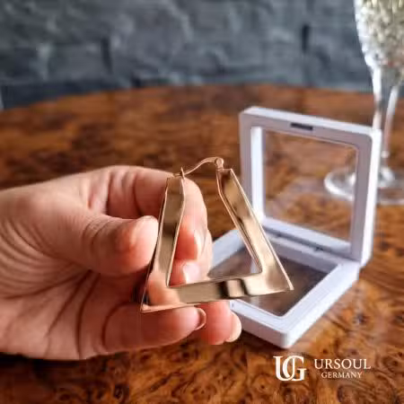 Aretes triángulo rosegold para mujer, Rosegold Color Ursoul Germany, en mano sobre mesa de madera