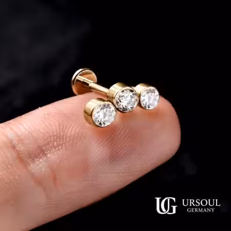 Piercing triple cristal dorado 8mm en cartílago para mujer, Gold Color Ursoul Germany, sobre dedo y fondo negro con detalle de rosca interna