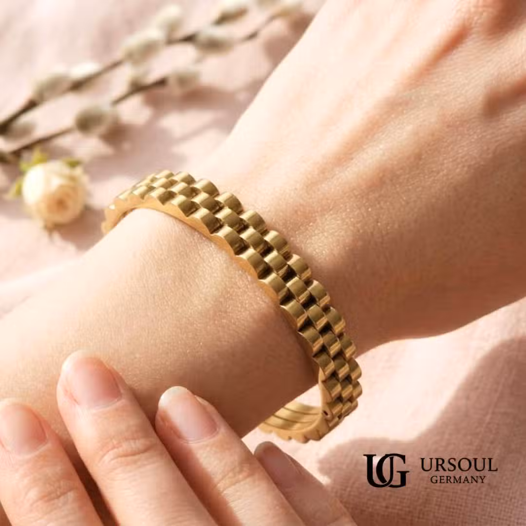 WhatsApp Image 2026-09-13 at 1.38.34 PM (2) Brazalete rígido dorado diseño presidencial para mujer, Gold Color Ursoul Germany, sobre mármol blanco y sobre muñeca con fondo floral rosa