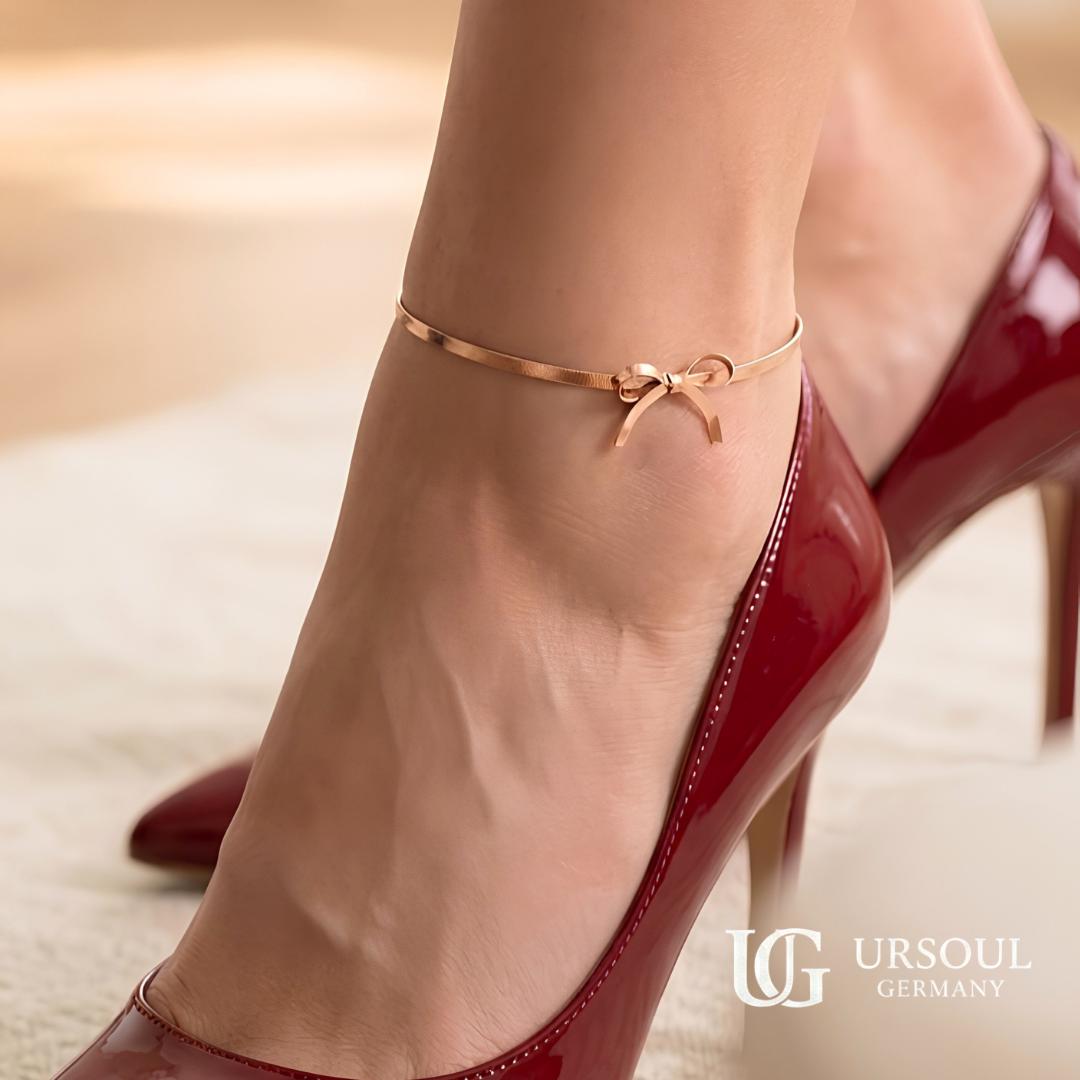WhatsApp Image 2026-09-13 at 1.38.34 PM (5) Tobillera color Rosegold con dije de moño y cadena tipo serpentina sobre tobillo de mujer, marca Ursoul Germany.