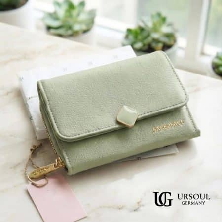 Billetera compacta color verde jade suave en piel vegana con broche dorado y etiqueta colgante, elegida por Ursoul Germany.