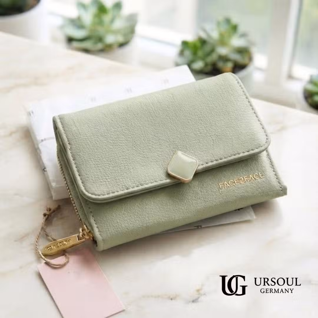 WhatsApp Image 2026-09-23 at 11.00.40 AM Billetera compacta color verde jade suave en piel vegana con broche dorado y etiqueta colgante, elegida por Ursoul Germany.