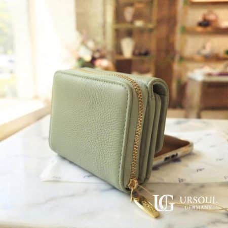 Billetera compacta color verde jade suave en piel vegana con broche dorado y etiqueta colgante, elegida por Ursoul Germany.